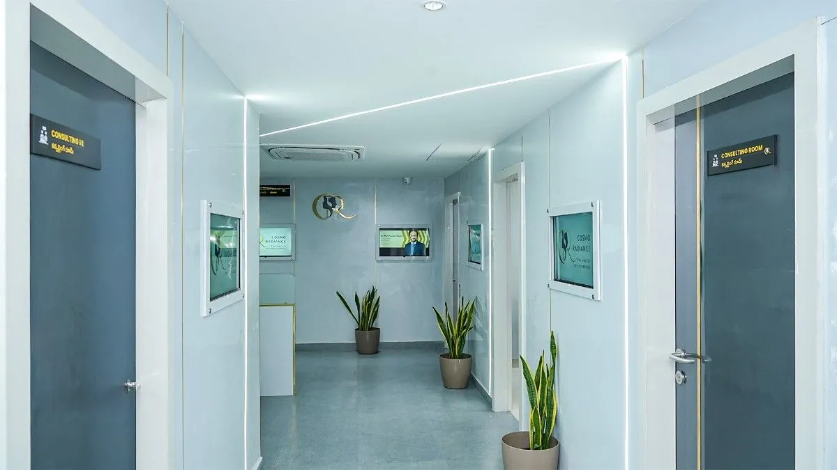 Brightly lit modern clinic corridor leading to the billing department and consultation rooms, decorated with potted snake plants along the grey and white walls.